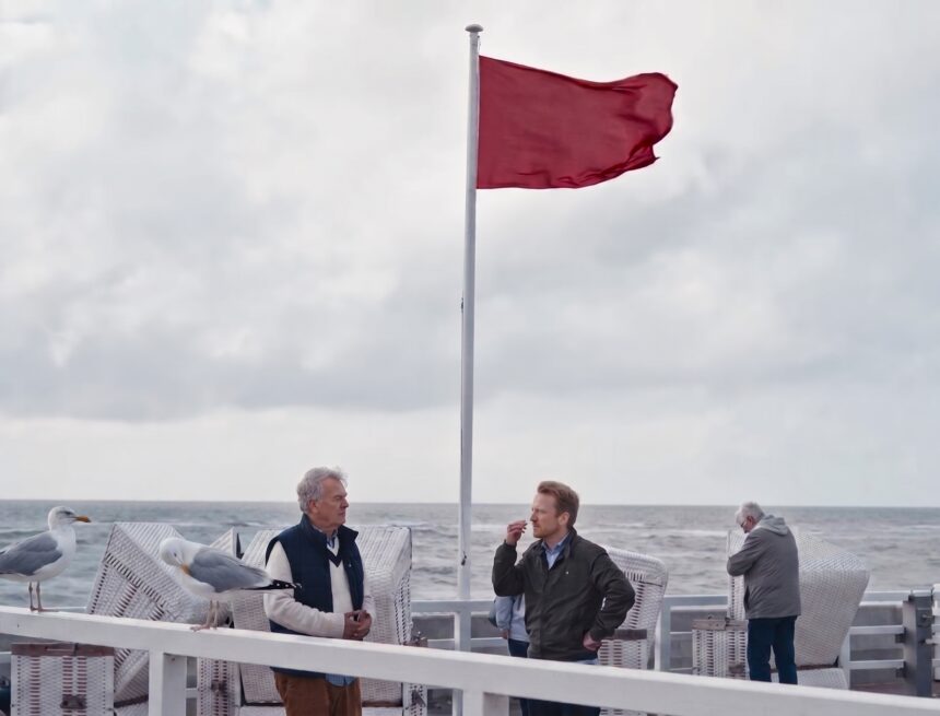 Zwei Möwen sitzen auf dem weißen Geländer der Westerländer Strandpromenade, dahinter Strandkörbe und die Nordsee