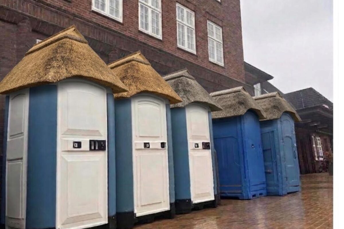 Die Reihe mobiler Toilettenkabinen vor dem Bahnhof Westerland auf Sylt, jede mit einer eigenen aufgesetzten Reetkappe.