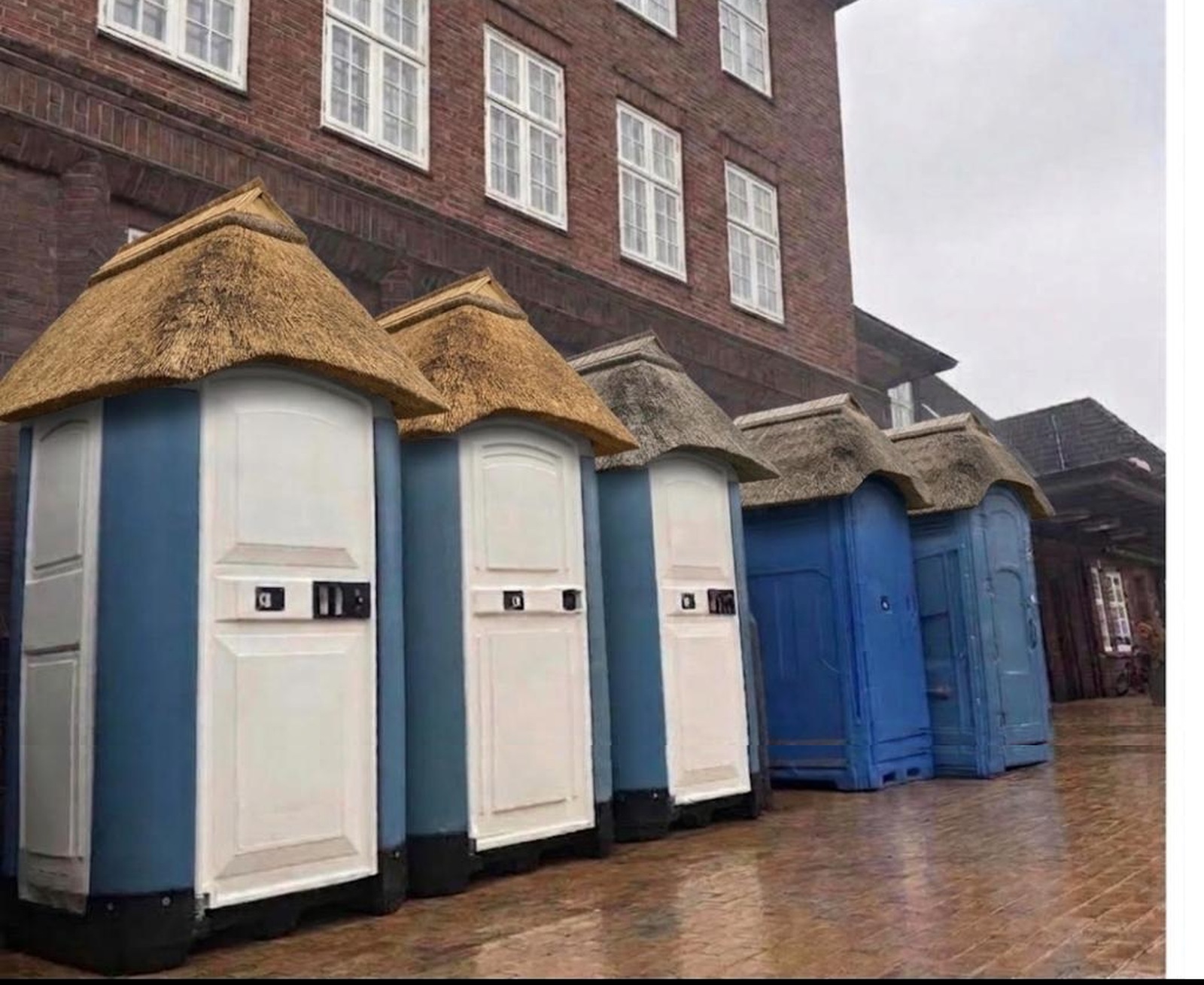 Die Reihe mobiler Toilettenkabinen vor dem Bahnhof Westerland auf Sylt, jede mit einer eigenen aufgesetzten Reetkappe.