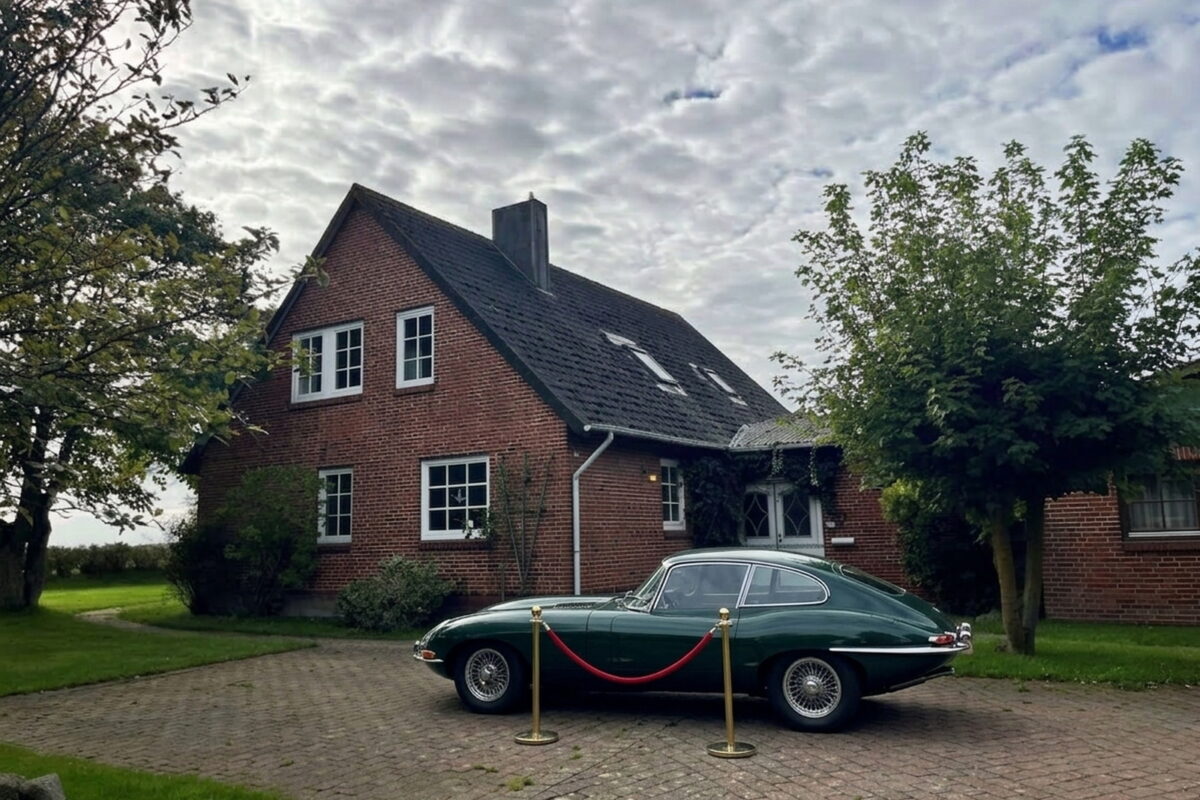 Dunkelgruener Oldtimer auf einem gepflasterten Hof vor einem Backsteinhaus auf Sylt, davor eine rote Museumskordel zwischen zwei Messingpfosten