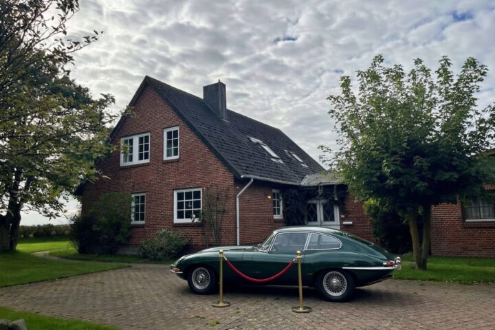 Dunkelgruener Oldtimer auf einem gepflasterten Hof vor einem Backsteinhaus auf Sylt, davor eine rote Museumskordel zwischen zwei Messingpfosten