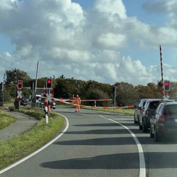 Bahnübergang in Keitum, ein Mitarbeiter in Warnkleidung hebt die Hand, dahinter wartende Autos