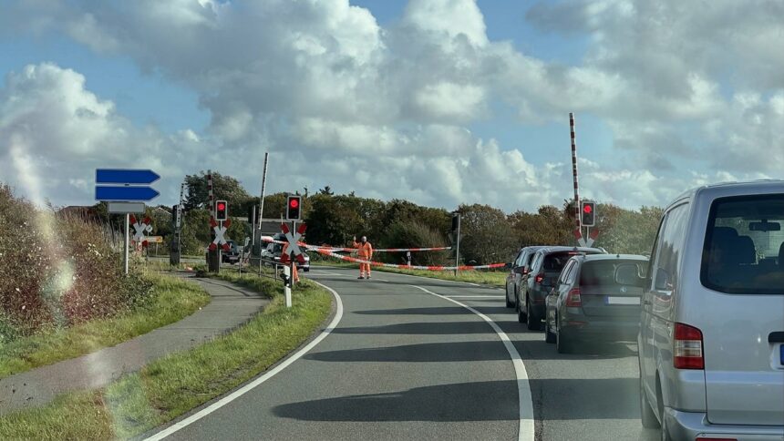 Bahnübergang Keitum mit Schrankenwärter Bahnübergang in Keitum, ein Mitarbeiter in Warnkleidung hebt die Hand, dahinter wartende Autos