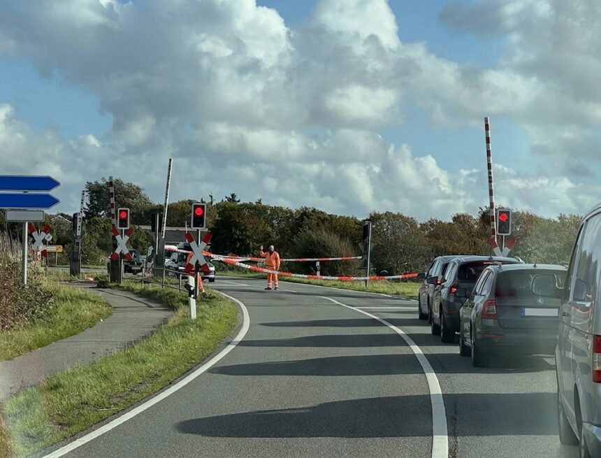 Bahnübergang in Keitum, ein Mitarbeiter in Warnkleidung hebt die Hand, dahinter wartende Autos
