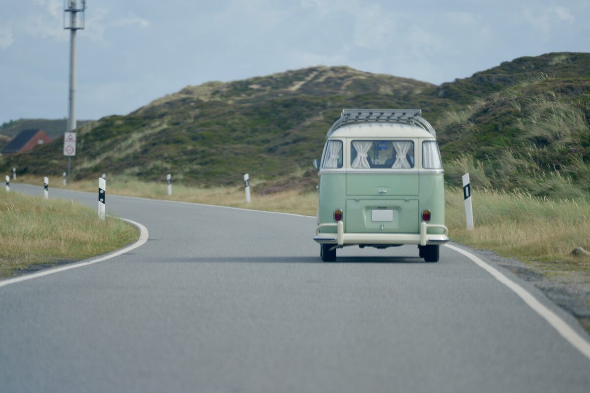 Grüner VW Bulli fährt auf einer Straße durch die Dünen auf Sylt