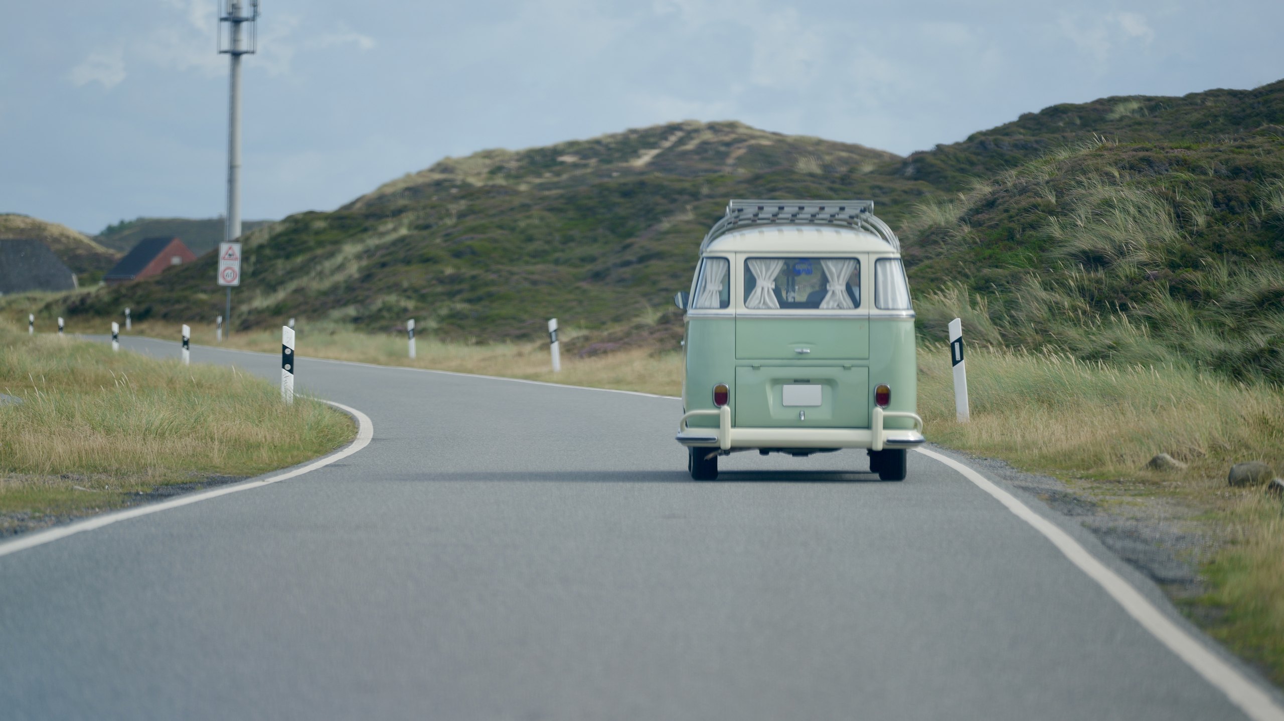 Grüner VW Bulli fährt auf einer Straße durch die Dünen auf Sylt